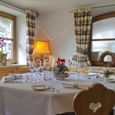 Stadlers Restaurant Gedeckter Esstisch mit weißer Tischdecke, Gläsern und Blumen vor großen Fenstern