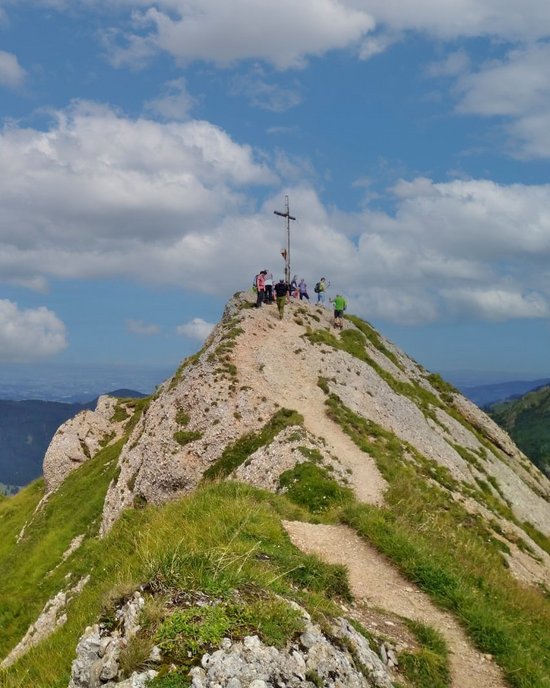 Berg mit Gipfelkreuz vor blauem Himmel